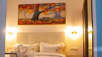 Habitación de hotel con una cama que presenta una disposición de almohadas en forma de corazón, un cuadro con árboles otoñales y luces fijadas a la pared.