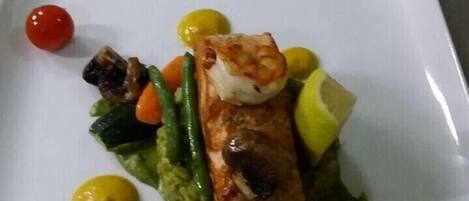 A plate of food with a piece of salmon, vegetables, and a lemon wedge.