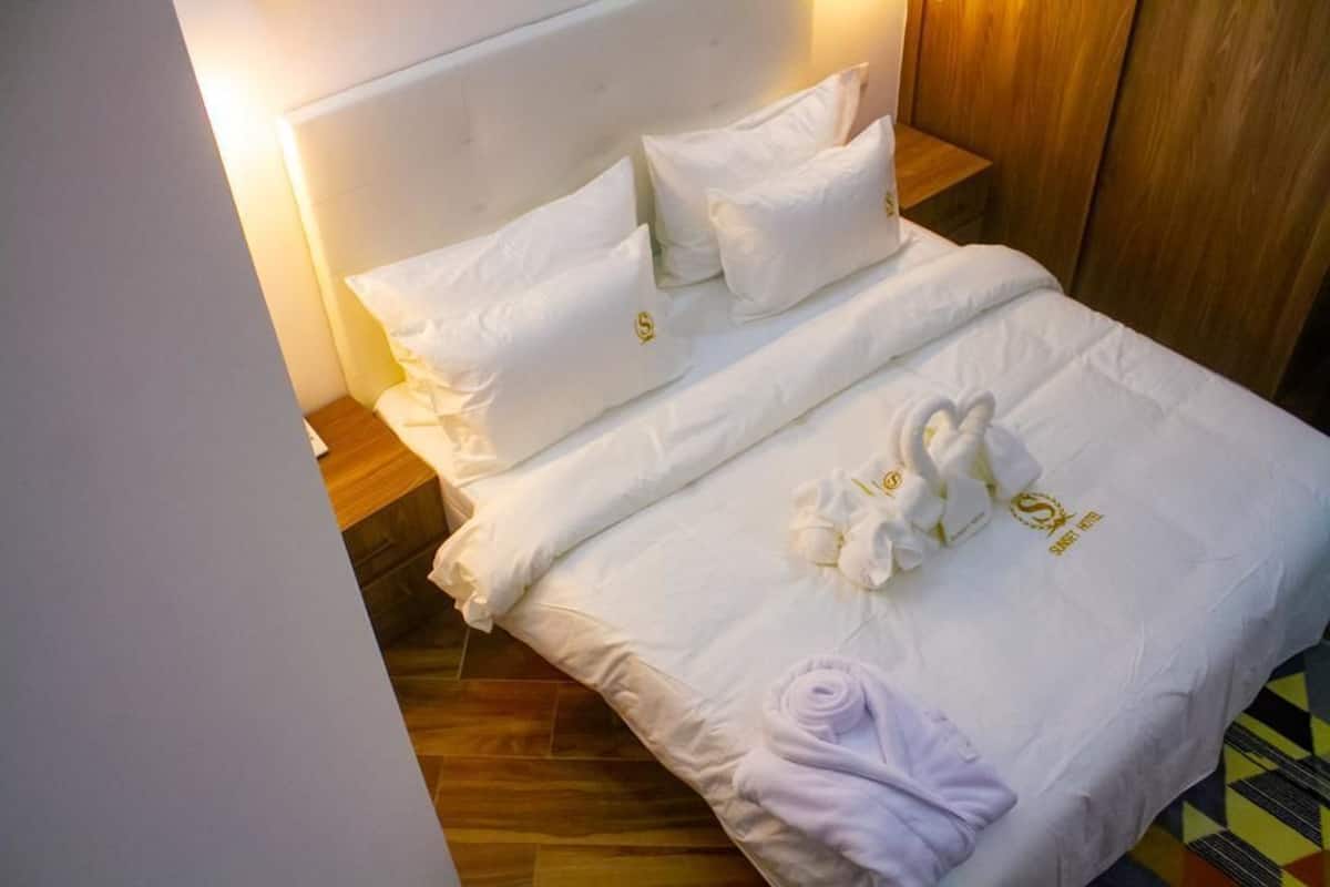 A neatly made bed with white linens, two pillows, and a set of towels.