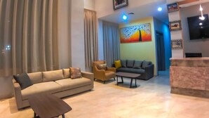 Una sala de estar moderna con sofá, sillón y una mesa de centro. Hay un cuadro en la pared y un televisor montado.