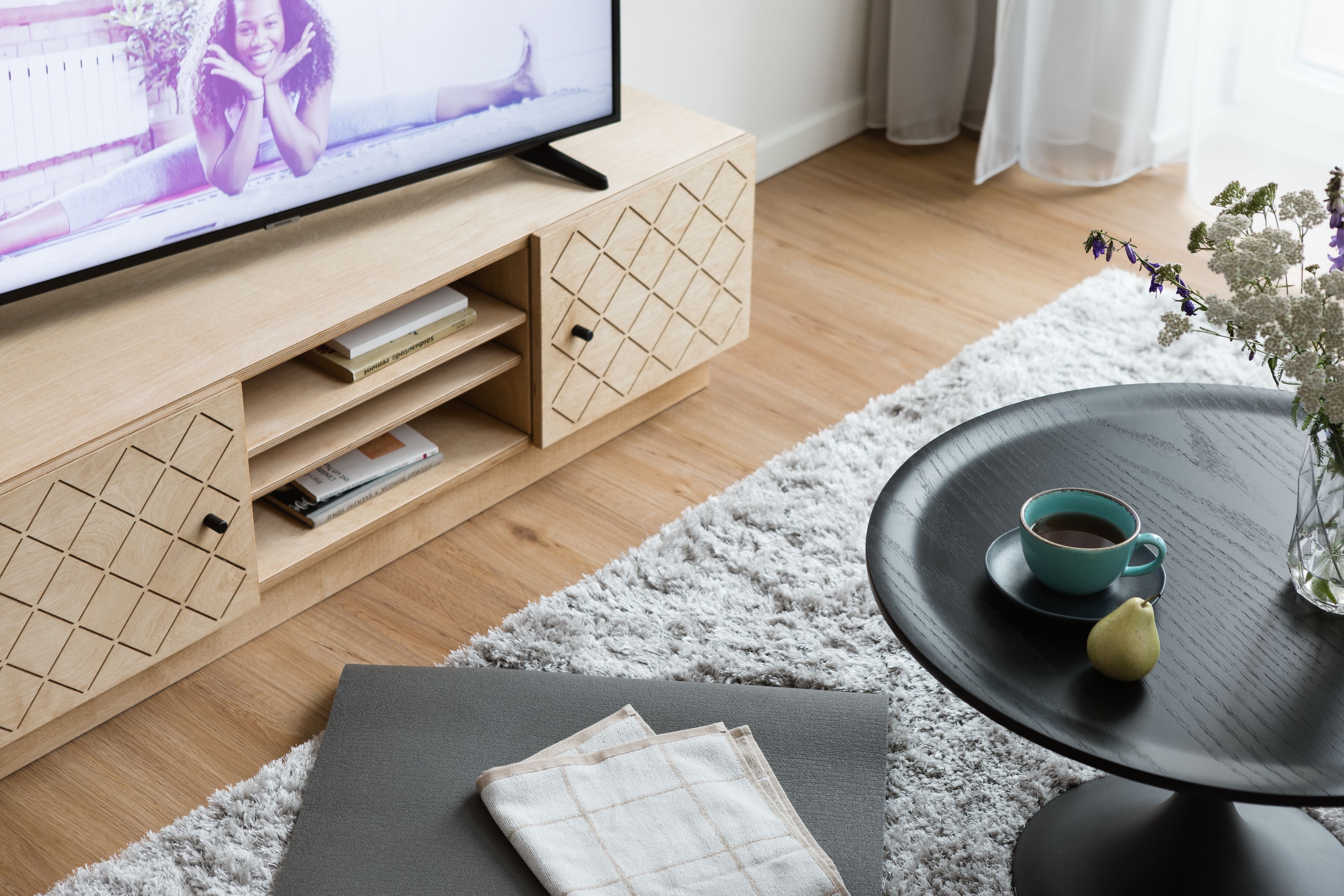 Ein modernes Wohnzimmer mit einer Holztrennwandschränke, einem schwarzen Couchtisch mit Tasse und Birne, und einem flauschigen weißen Teppich.