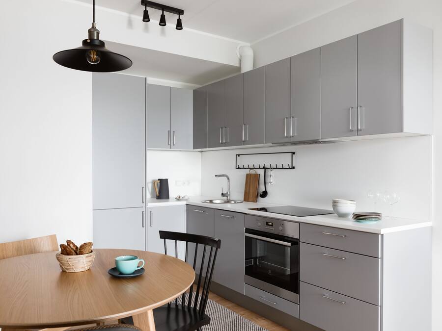 A modern kitchen with grey cabinets, a wooden dining table, and a hanging light fixture.