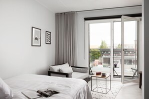 A modern hotel room with a bed, a sofa, a small table, and a balcony with a view of buildings. - Bob W Tallinn Telliskivi (Tallinn)