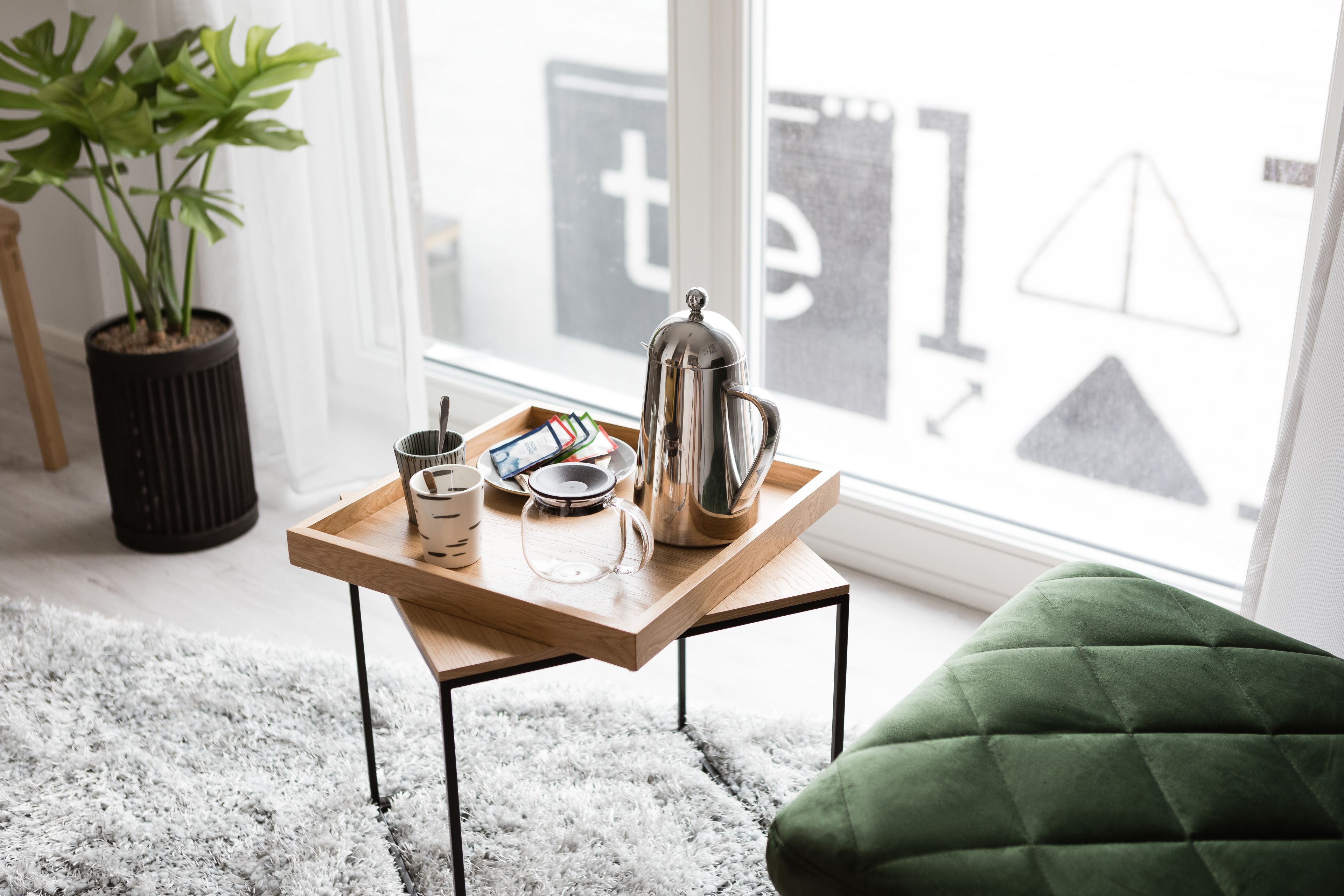 A wooden table with a tray holding a coffee pot, a mug, and a smartphone. A green chair is visible in the foreground.