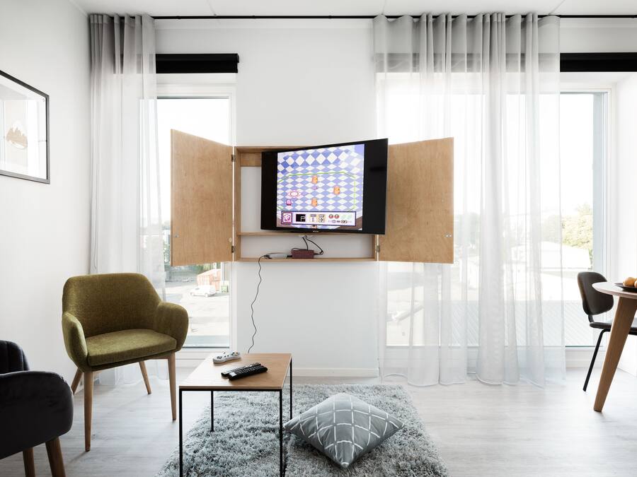 Ein modernes Wohnzimmer mit Wand-Fernseher, Couchtisch aus Holz, einer Couch und einem Essbereich mit Tisch und Stühlen.