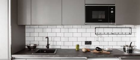 A modern kitchen with grey cabinets, a Bosch microwave, a built-in washing machine, and a tiled backsplash.