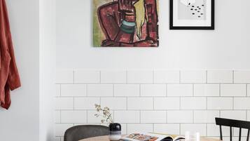 A dining area with a round table, two chairs, a hanging pendant light, and artwork on the wall.