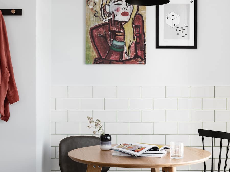 Un comedor con una mesa redonda, dos sillas, una lámpara colgante y una obra de arte en la pared.