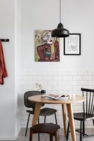 Een eetgedeelte met een ronde tafel, twee stoelen, een hangende hanglamp en kunst aan de muur.
