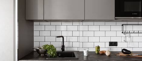 A modern kitchen with a black sink, white tiles, a Bosch oven, and a countertop with a cutting board, knife, and vegetables.