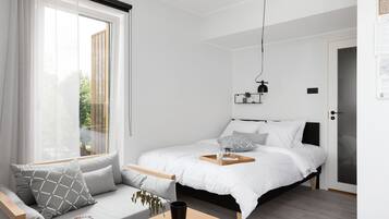 A modern bedroom with a bed, a sofa, a bedside table, and a window with curtains.