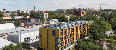 A yellow multi-story building with a flat roof, surrounded by greenery and other buildings.