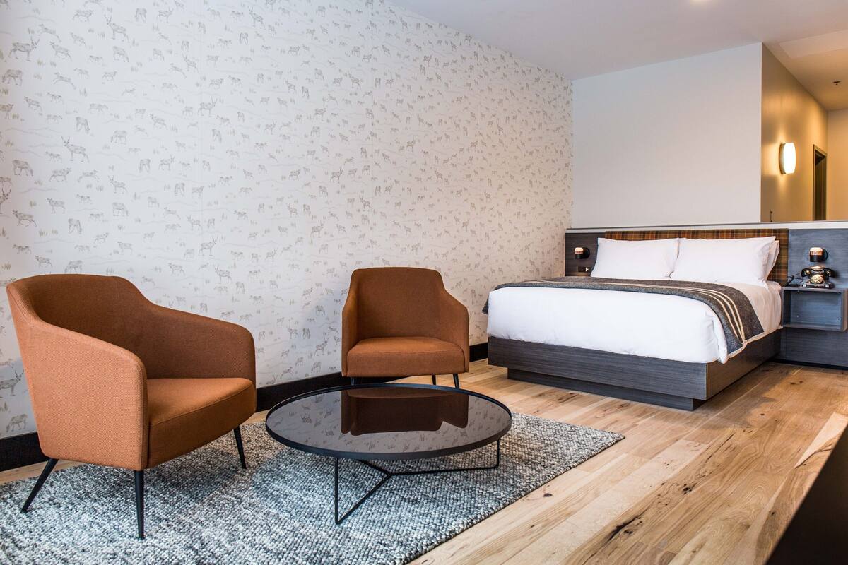 Ein Hotelzimmer mit einem Bett, zwei Sesseln, einem kleinen runden Tisch und einer Wand mit Muster.