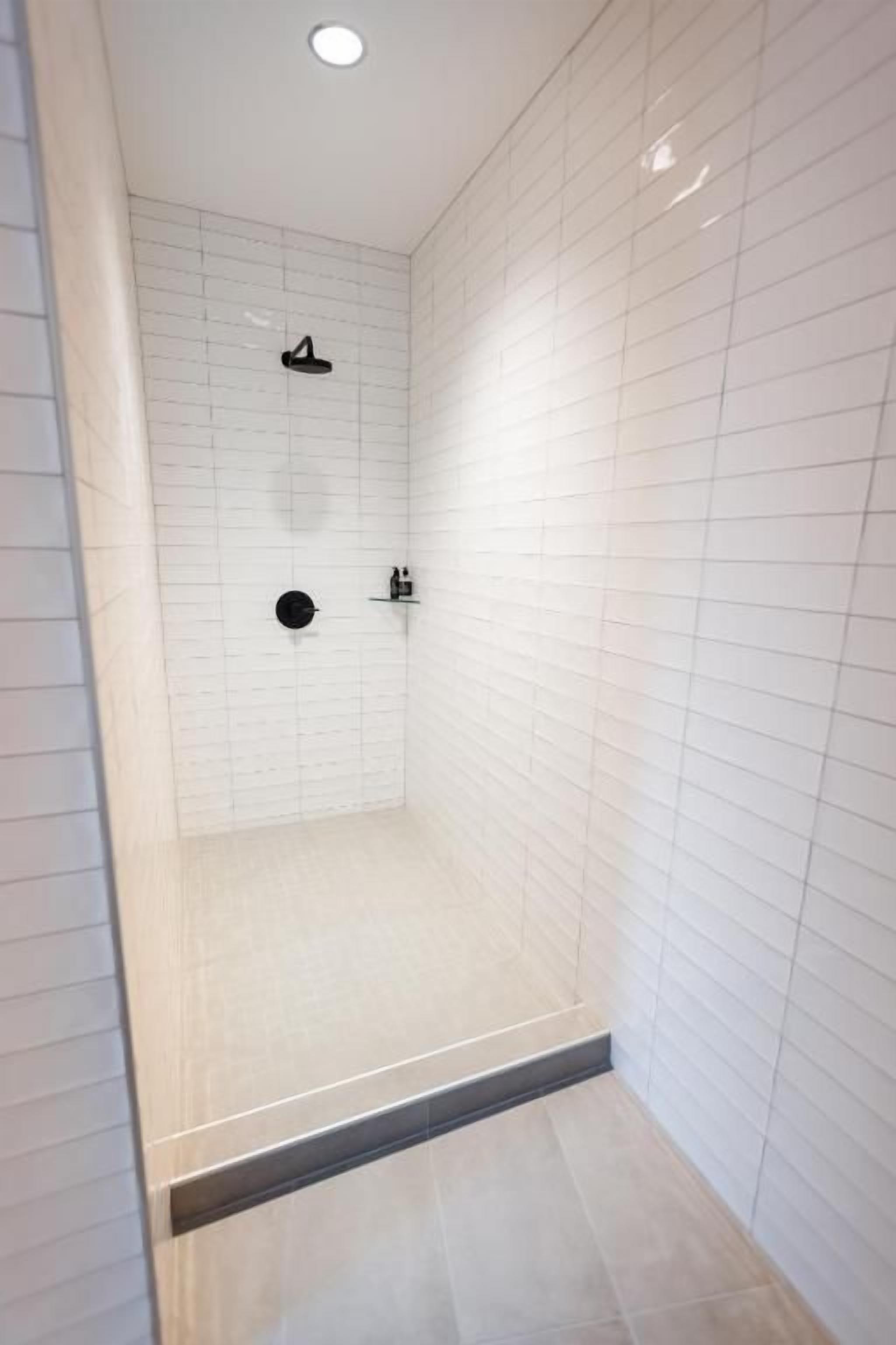 A shower with white tiled walls and a tiled floor.