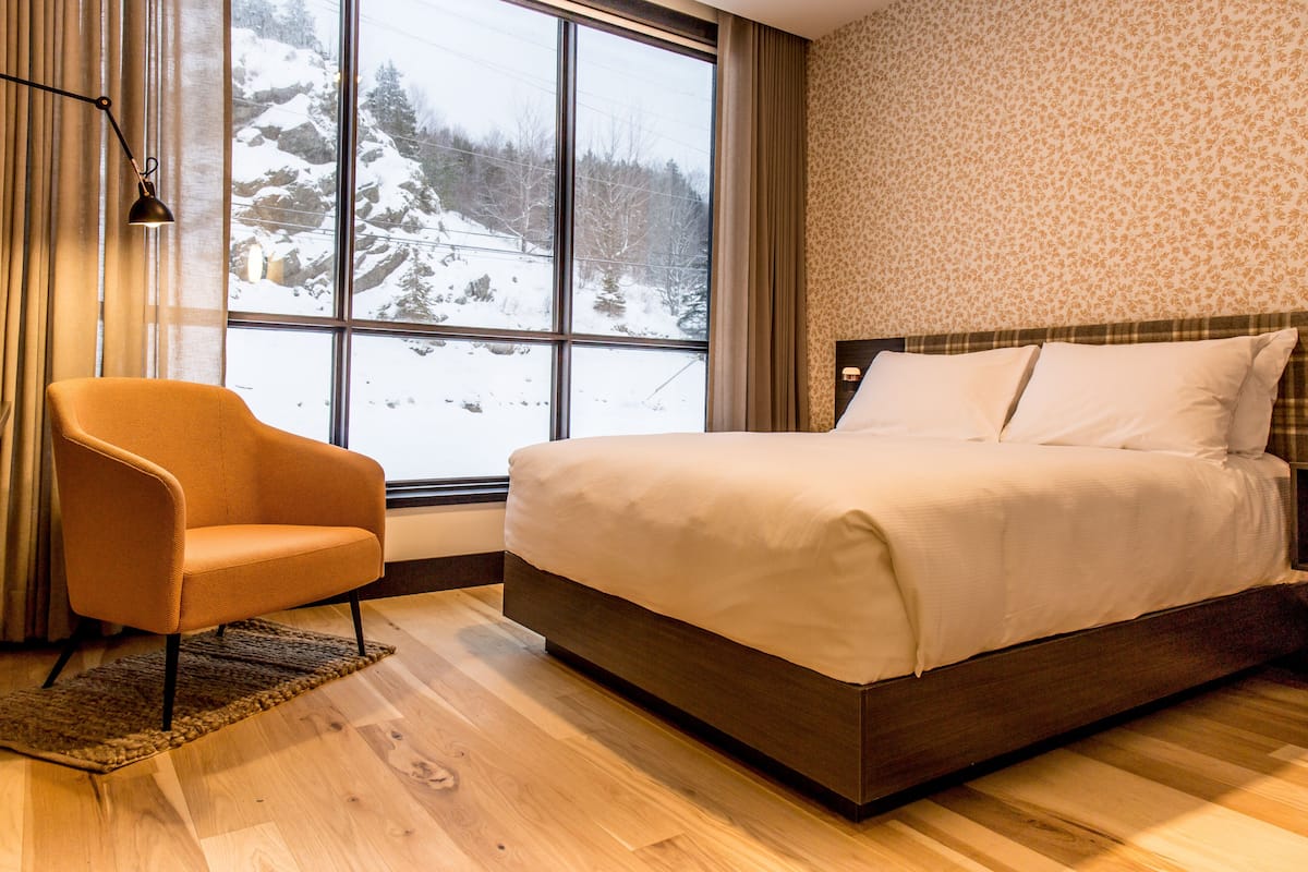 Ein Schlafzimmer mit großem Fenster, einem Bett, einem Sessel und einer Wand mit Muster.