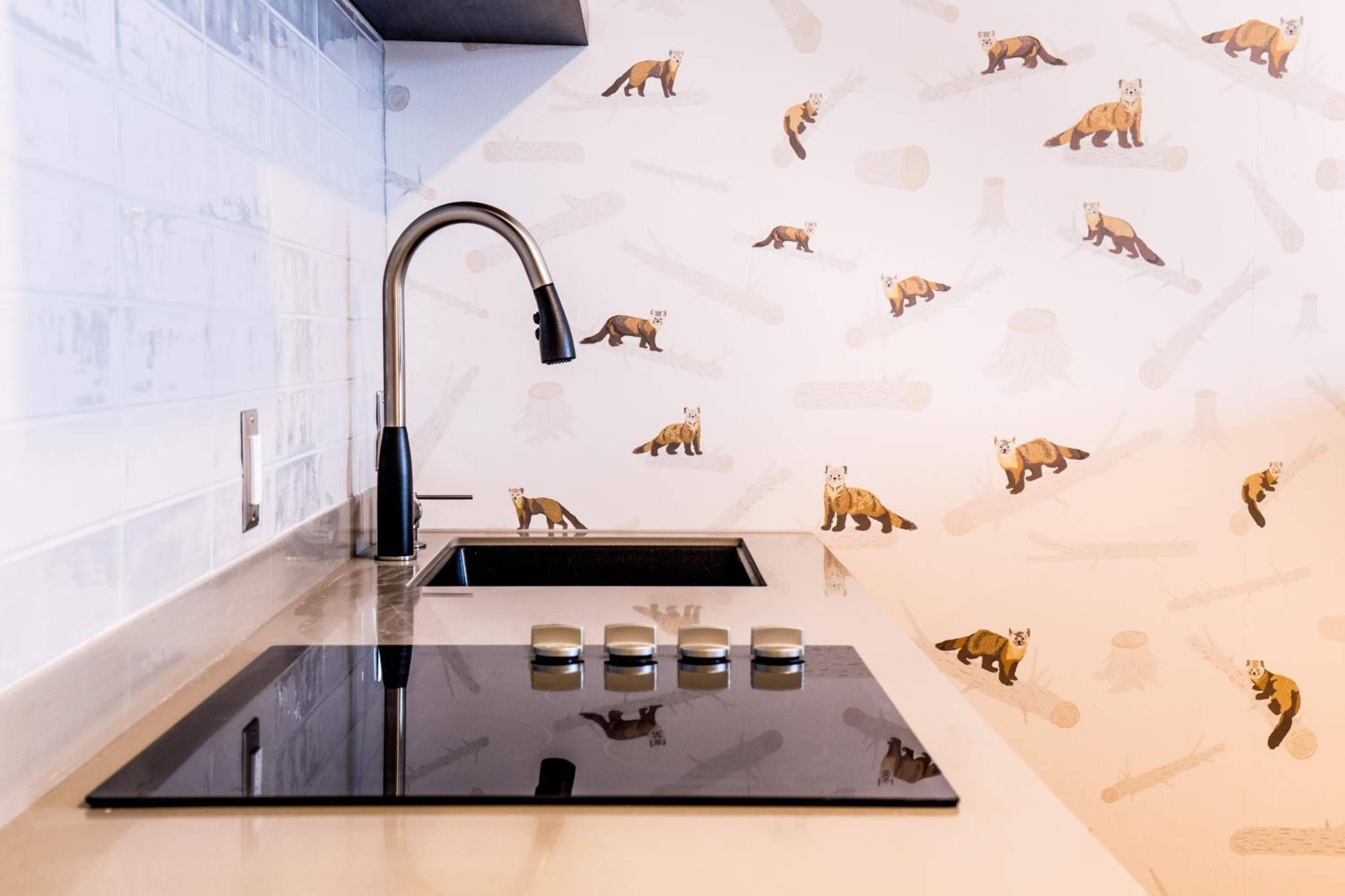 Una cocina con un lavamanos moderno, un grifo y un protector contra salpicaduras con diseños de animales.