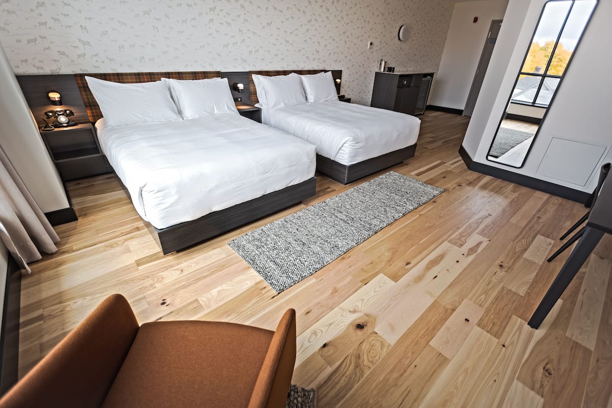 Ein modernes Schlafzimmer mit zwei Betten, Holzboden, grauem Teppich und Blick ins Freie.