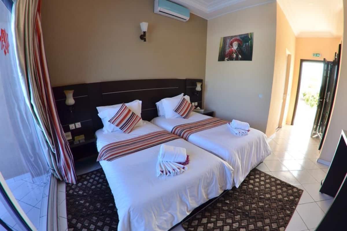 A hotel room with two beds, a patterned rug, and a painting on the wall.