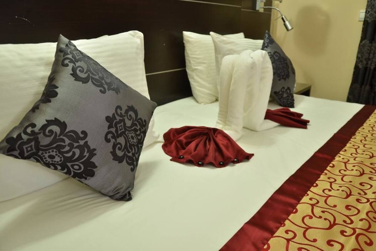 A neatly made bed with white and gray patterned pillows, a red cloth, and a red and gold bed runner.
