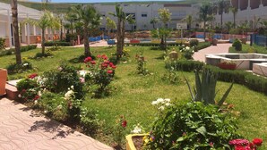 A courtyard with a pool, palm trees, and a variety of flowers. - Motel Al Akha (Ain Kansra)