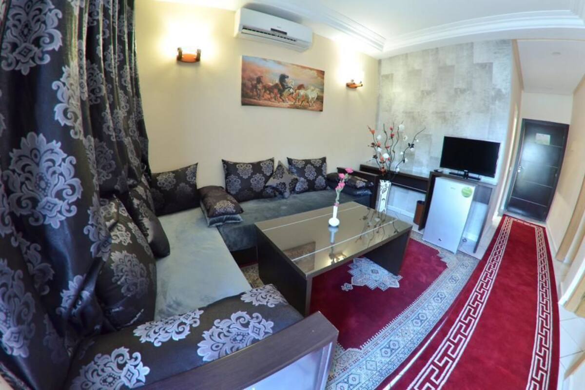 A living room with a sofa set, a coffee table, a TV, and a kitchen area.