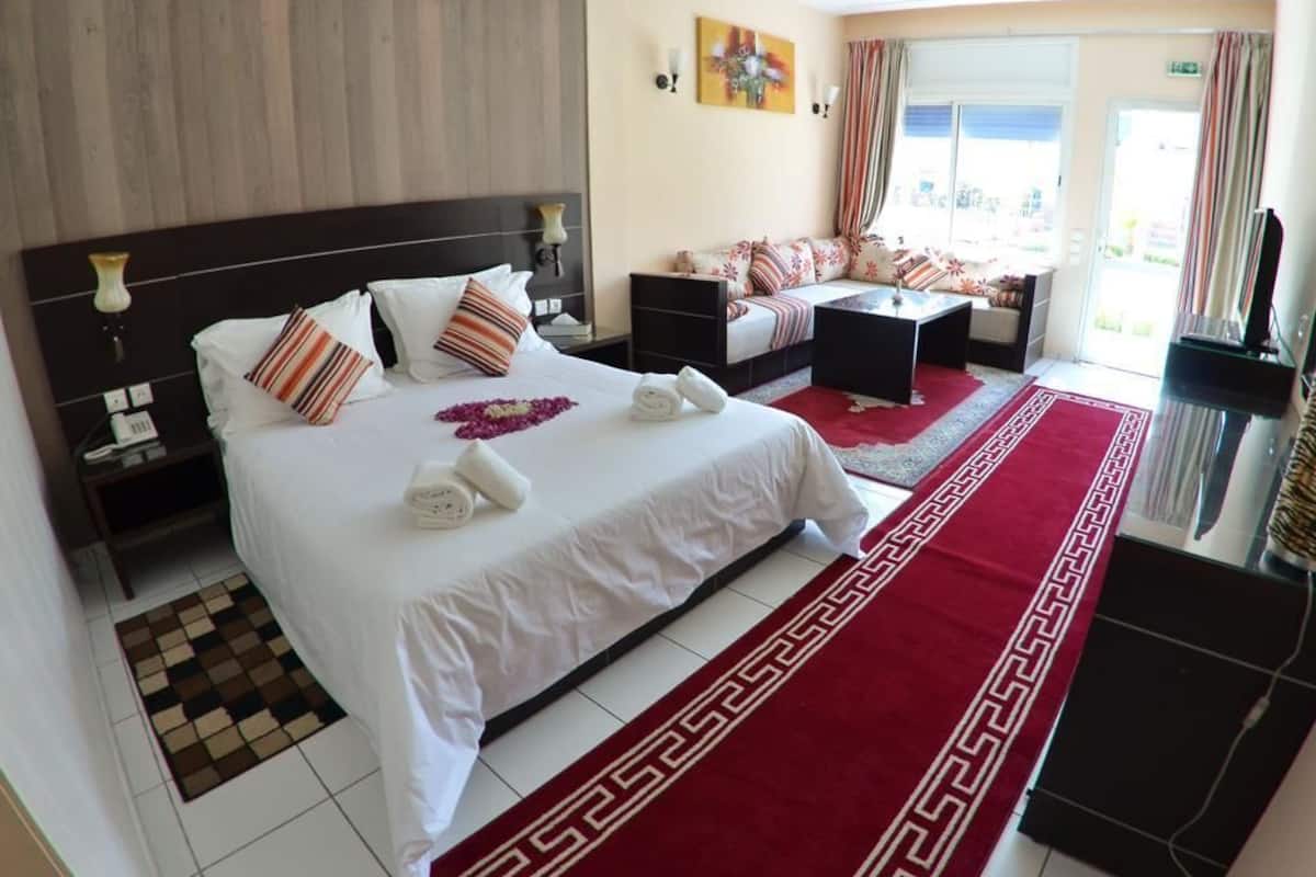 A hotel room with a large bed, a sofa, a small table, and a TV.