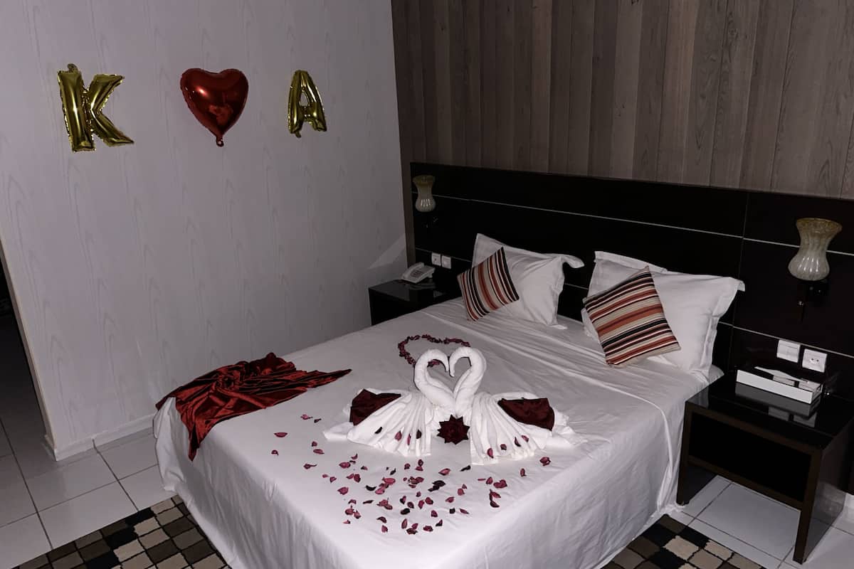 A neatly made bed with white linens, a heart-shaped balloon, and the letters "K" and "A" in gold.
