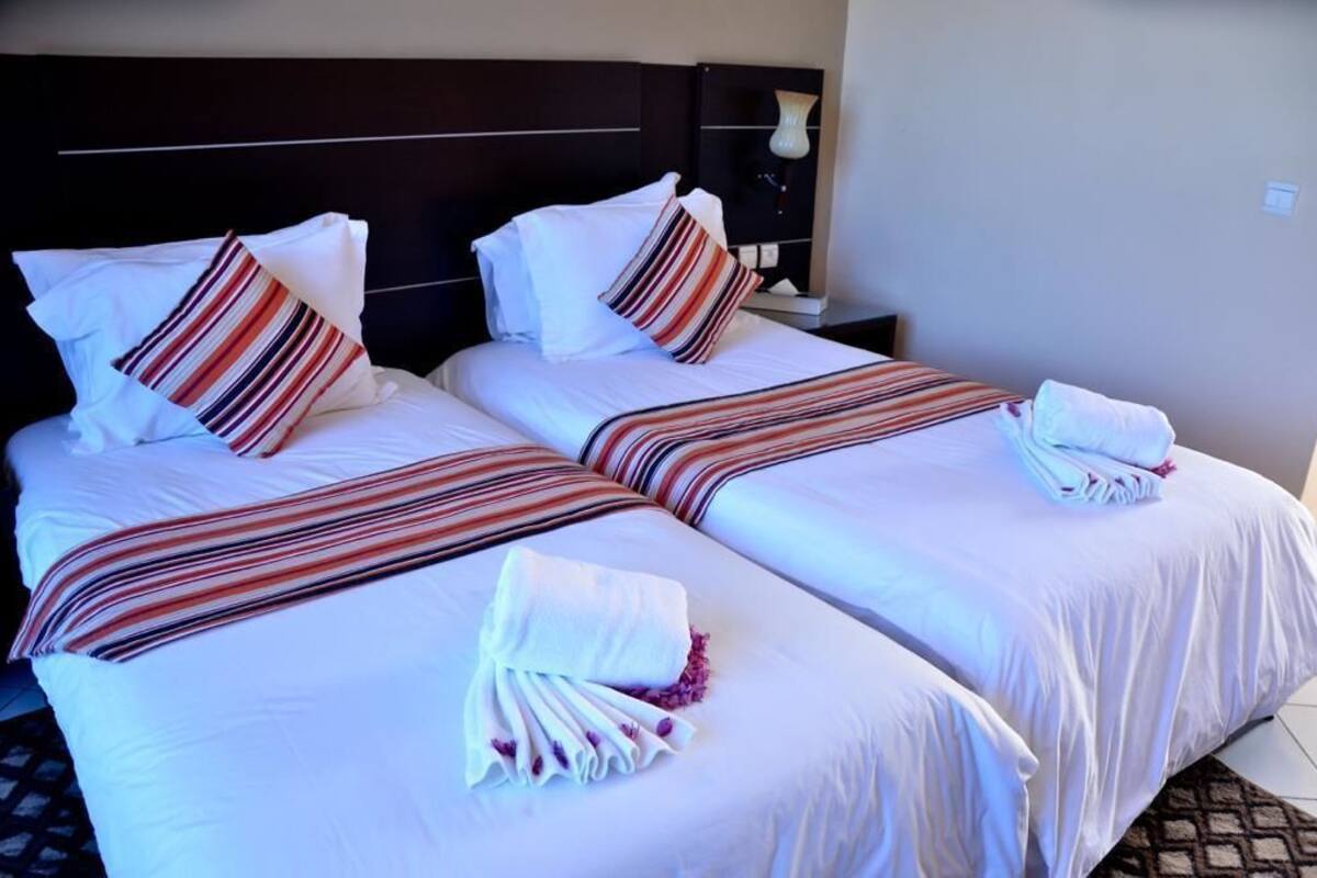 A hotel room with two beds, each with striped bedding and pillows, a nightstand with a lamp, and a headboard.