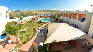 A hotel courtyard with a swimming pool, outdoor seating, and a large umbrella. - Motel Al Akha (Ain Kansra)