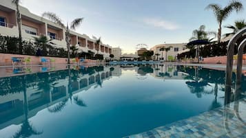 Una piscina al aire libre, sombrillas, sillones reclinables de piscina