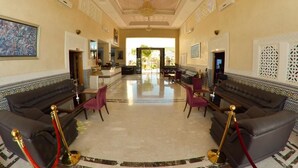 A spacious lobby with a high ceiling, ornate ceiling design, and a chandelier. There are two sofas and a dining area with chairs. - Motel Al Akha (Ain Kansra)