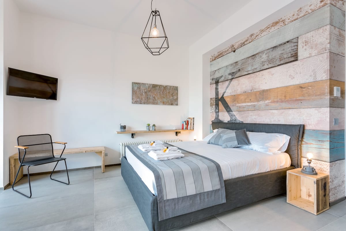 Ein modernes Schlafzimmer mit Bett, Nachttisch, Sessel und einem Kunstwerk an der Wand.
