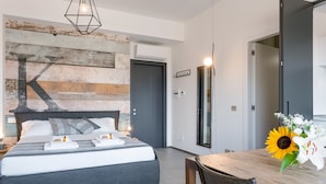 A modern bedroom with a large bed, a wooden accent wall, a dining table with a vase of flowers, and a mirror. - Rome as you feel - San Lucio Apartments (Rome)