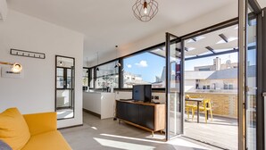 A modern living room with a sofa, a television on a wooden cabinet, and a large sliding glass door leading to a balcony with outdoor furniture. - Rome as you feel - San Lucio Apartments (Rome)