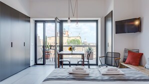 A modern bedroom with a large bed, a TV mounted on the wall, and a balcony with a table and chairs. - Rome as you feel - San Lucio Apartments (Rome)