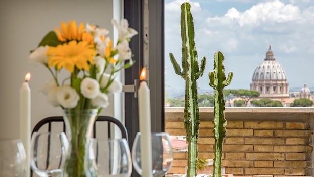 A dining table with a vase of flowers and candles, a cactus plant, and a view of a dome building. - Rome as you feel - San Lucio Apartments (Rome)