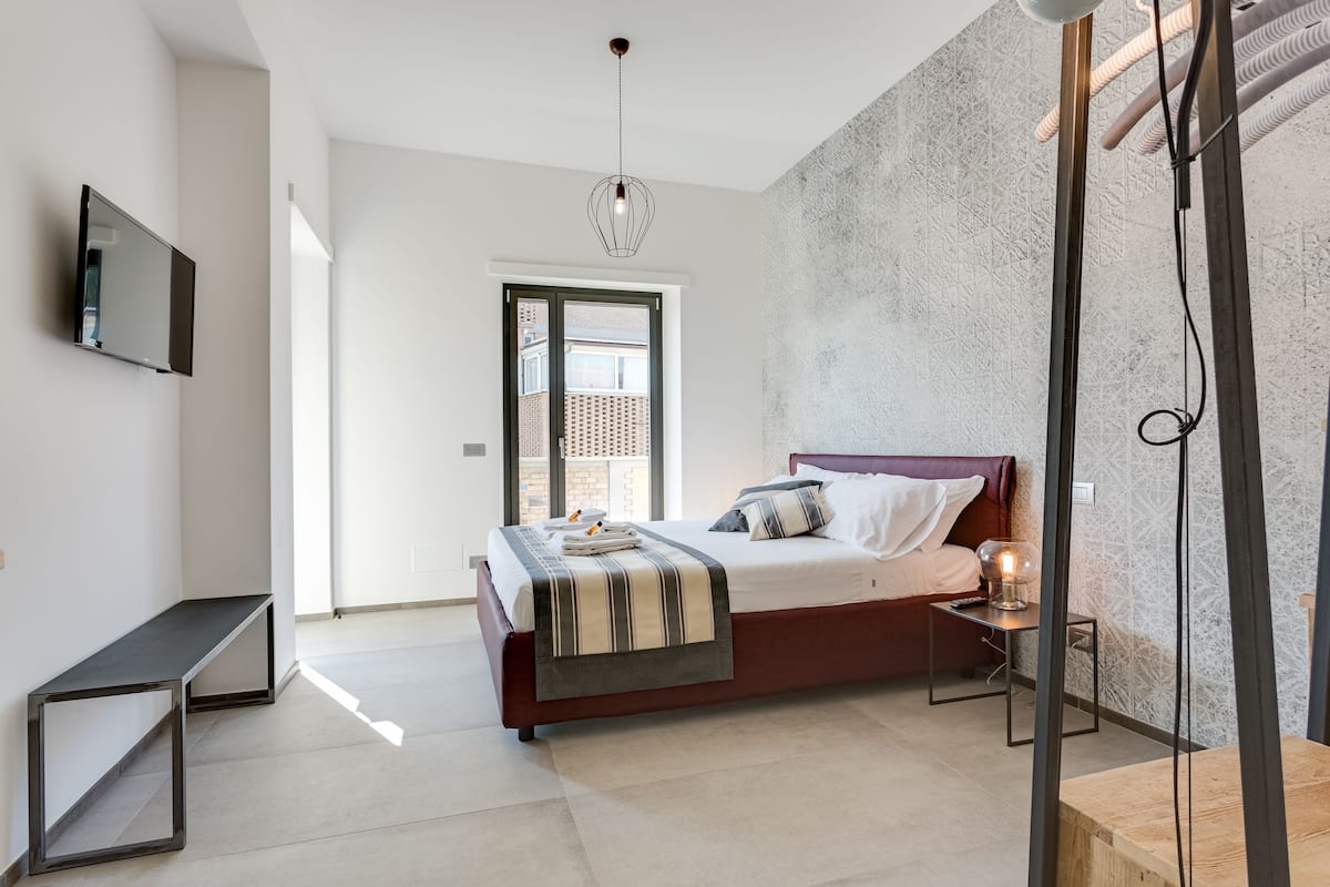 Ein modernes Schlafzimmer mit Bett, Nachttisch und einem an der Wand montierten Fernseher.