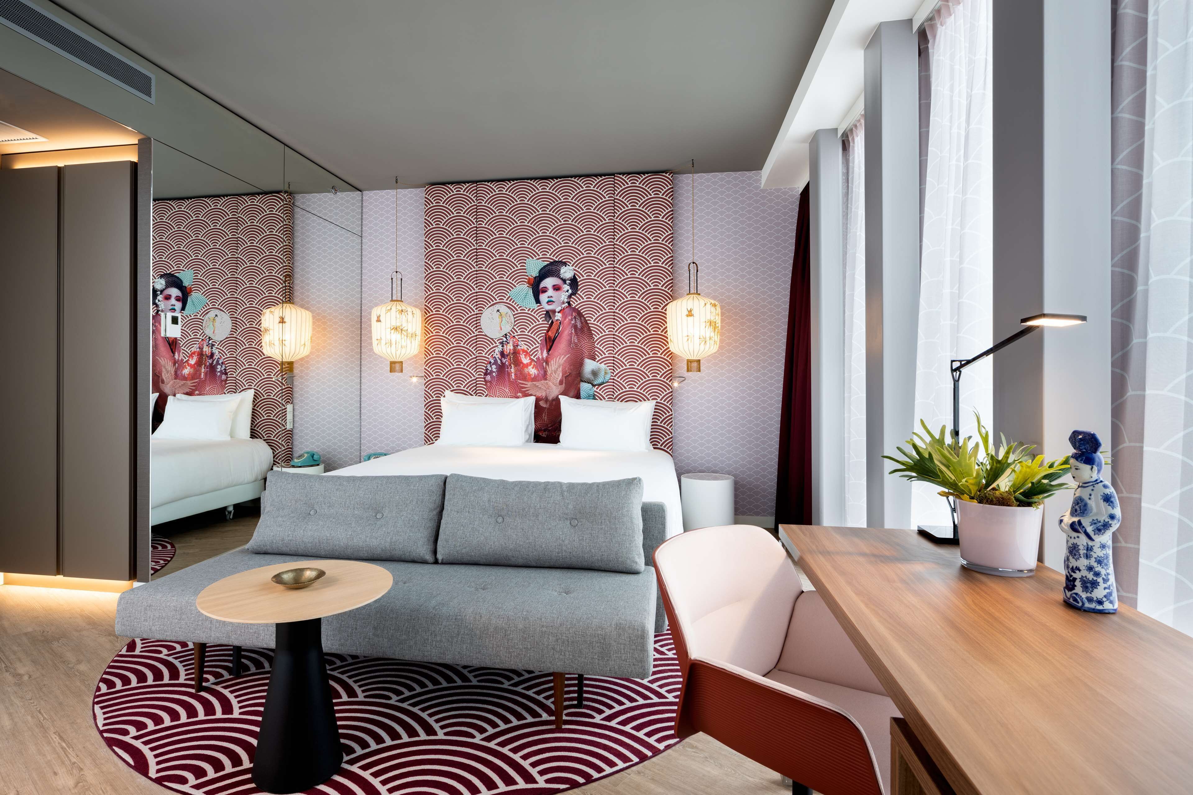 A modern hotel room with a bed, sofa, dining table, and decorative wall art.