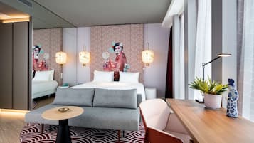 A modern hotel room with a bed, sofa, dining table, and decorative wall art.