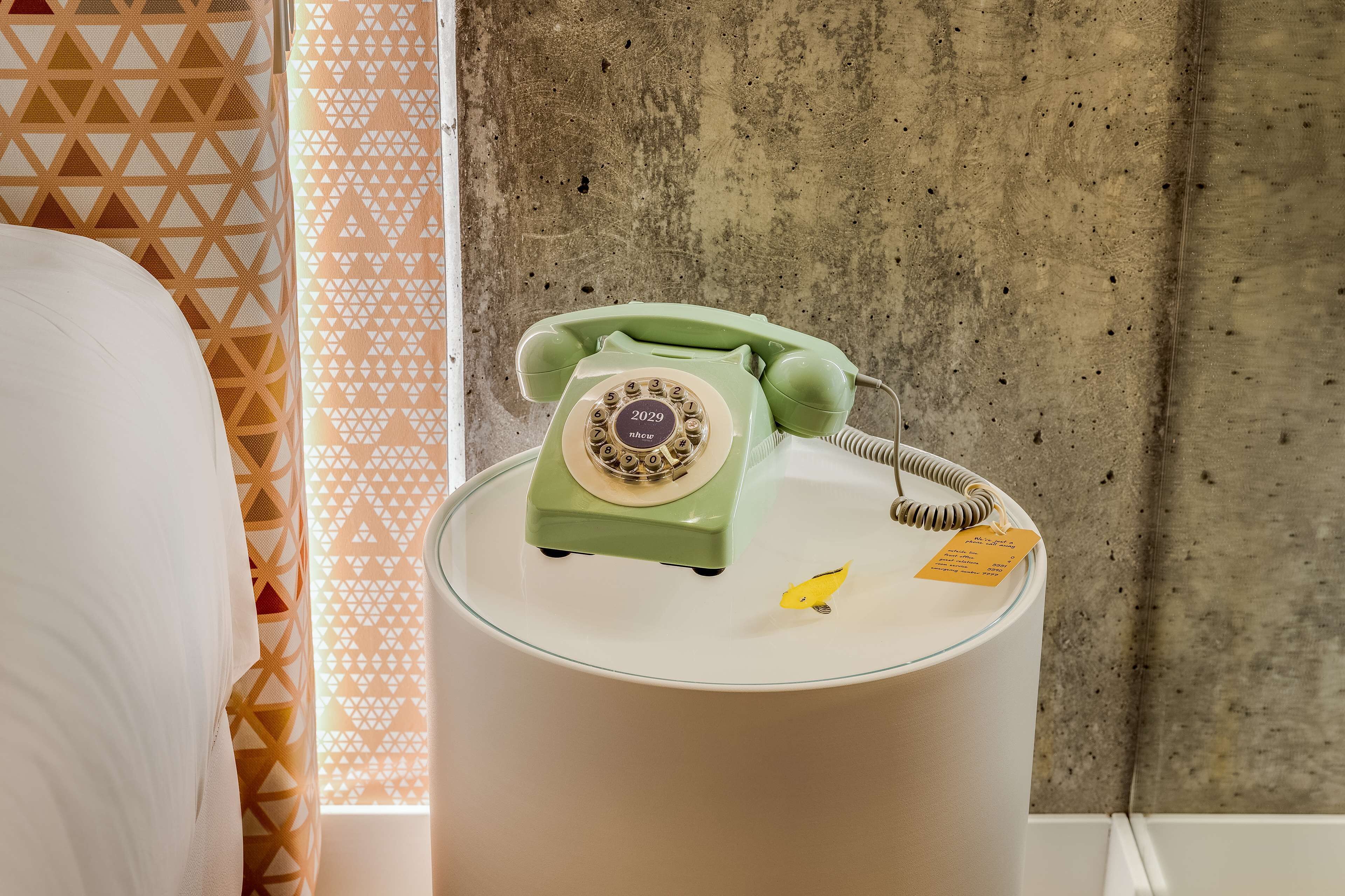 Ein grünes Wählscheibentelefon auf einem weißen Nachttisch in einem Hotelzimmer.