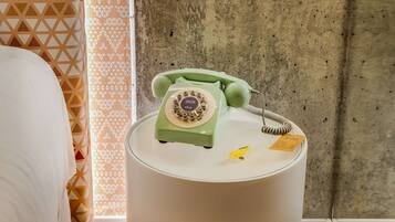 Un teléfono giratorio verde sobre una mesita de noche blanca en una habitación de hotel.