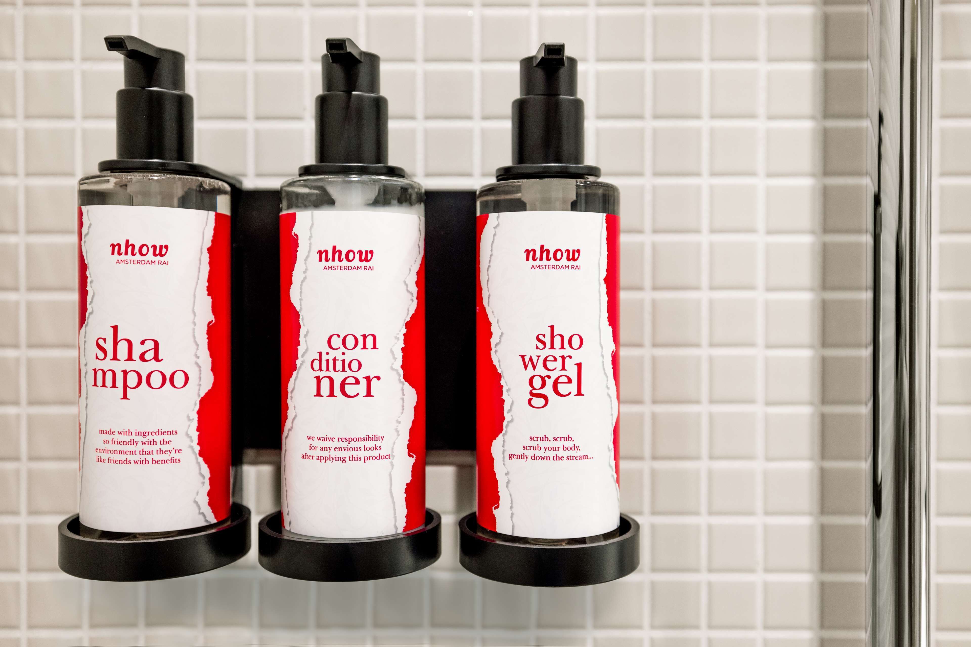 Tres botellas de champú, acondicionador y gel de ducha Nhow sobre un soporte negro frente a una pared de azulejos.