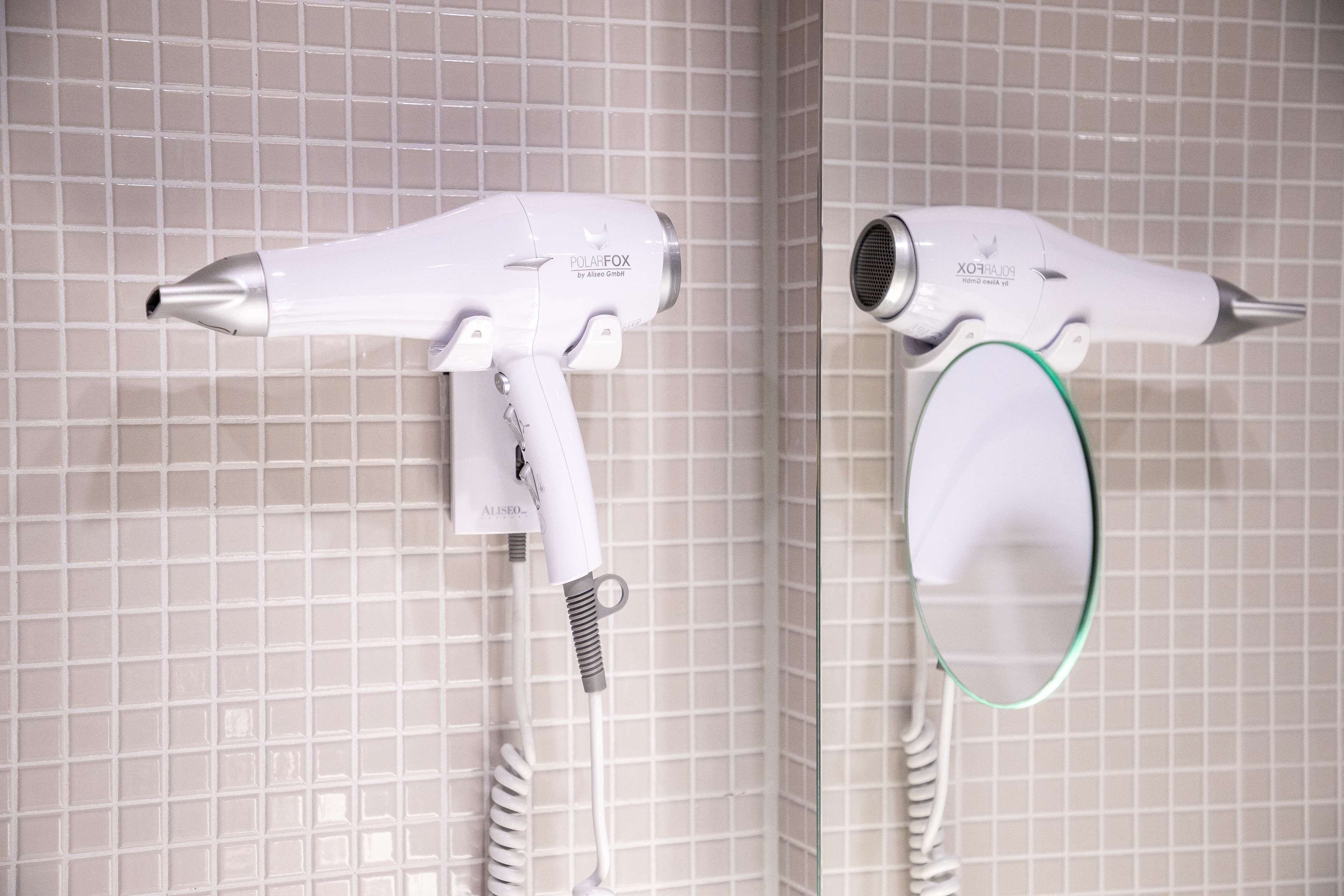 Two hair dryers mounted on a tiled wall.