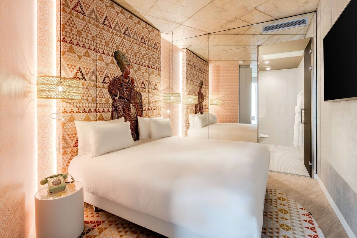 A modern hotel room with a large bed, a patterned wall, and a television.