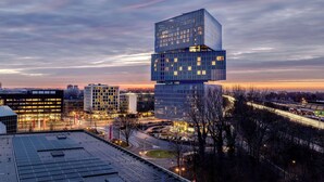 A modern building with a unique stacked design, surrounded by a cityscape and a highway. - nhow Amsterdam RAI (Amsterdam)