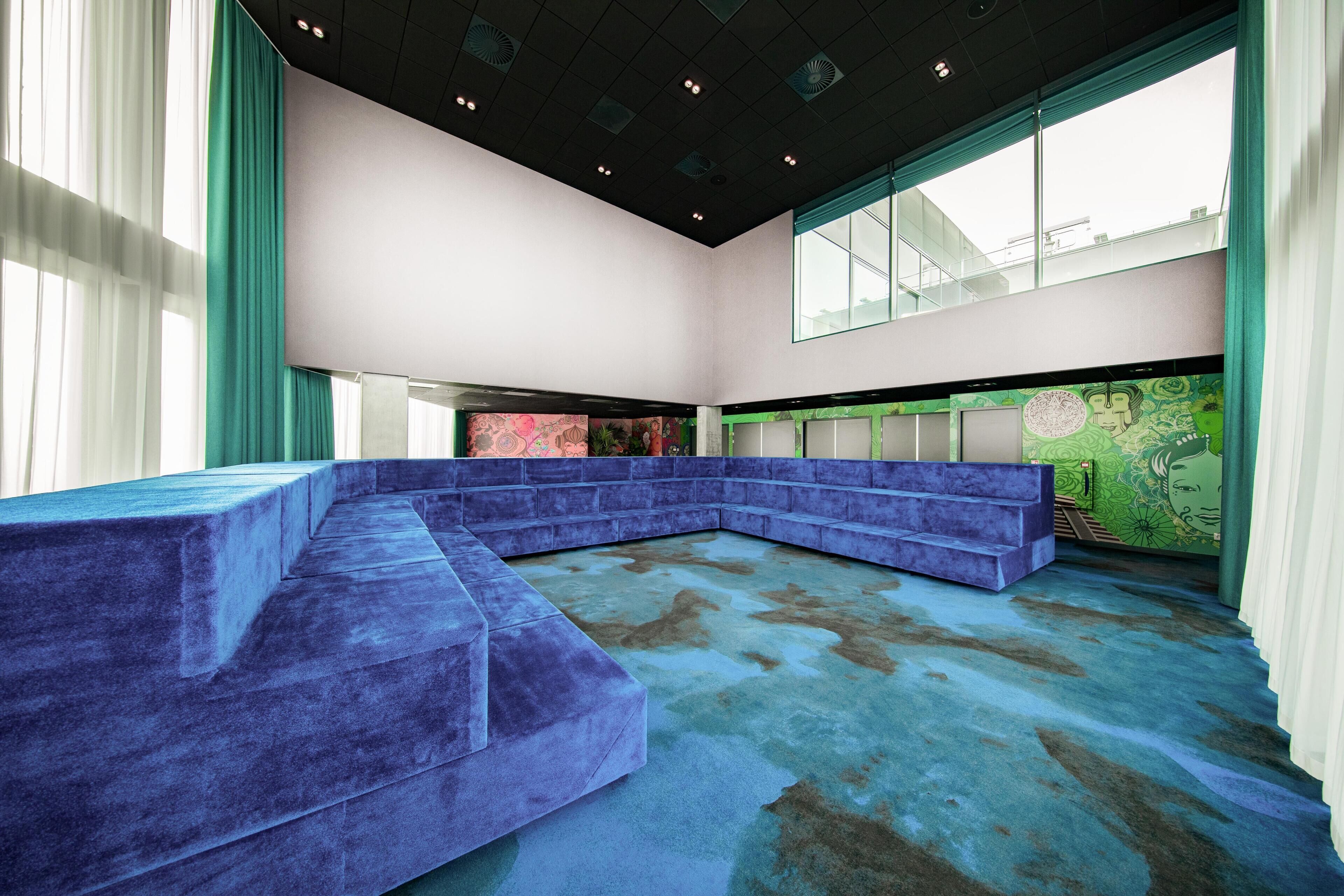 A modern interior with a blue seating area, large windows, and a green wall with artwork.