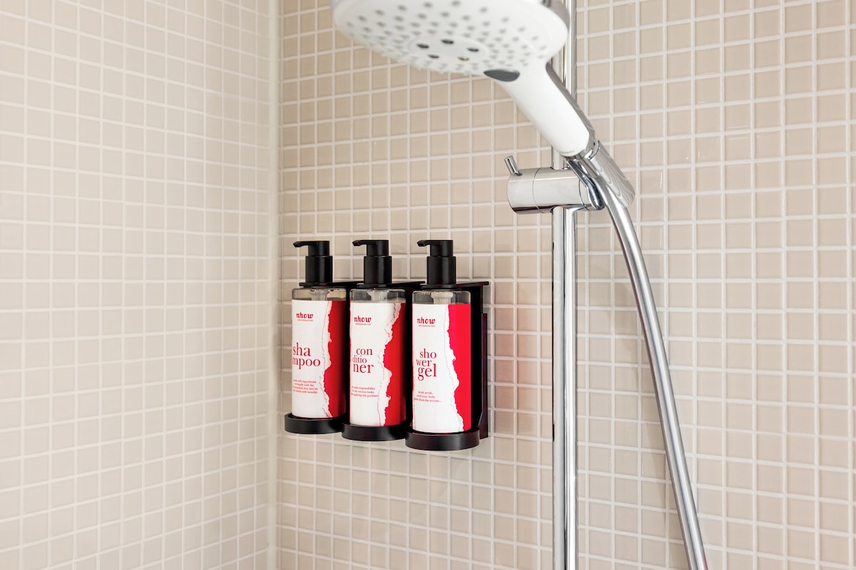 Ducha con cabezal de ducha manual y tres botellas de champú y acondicionador en la pared.