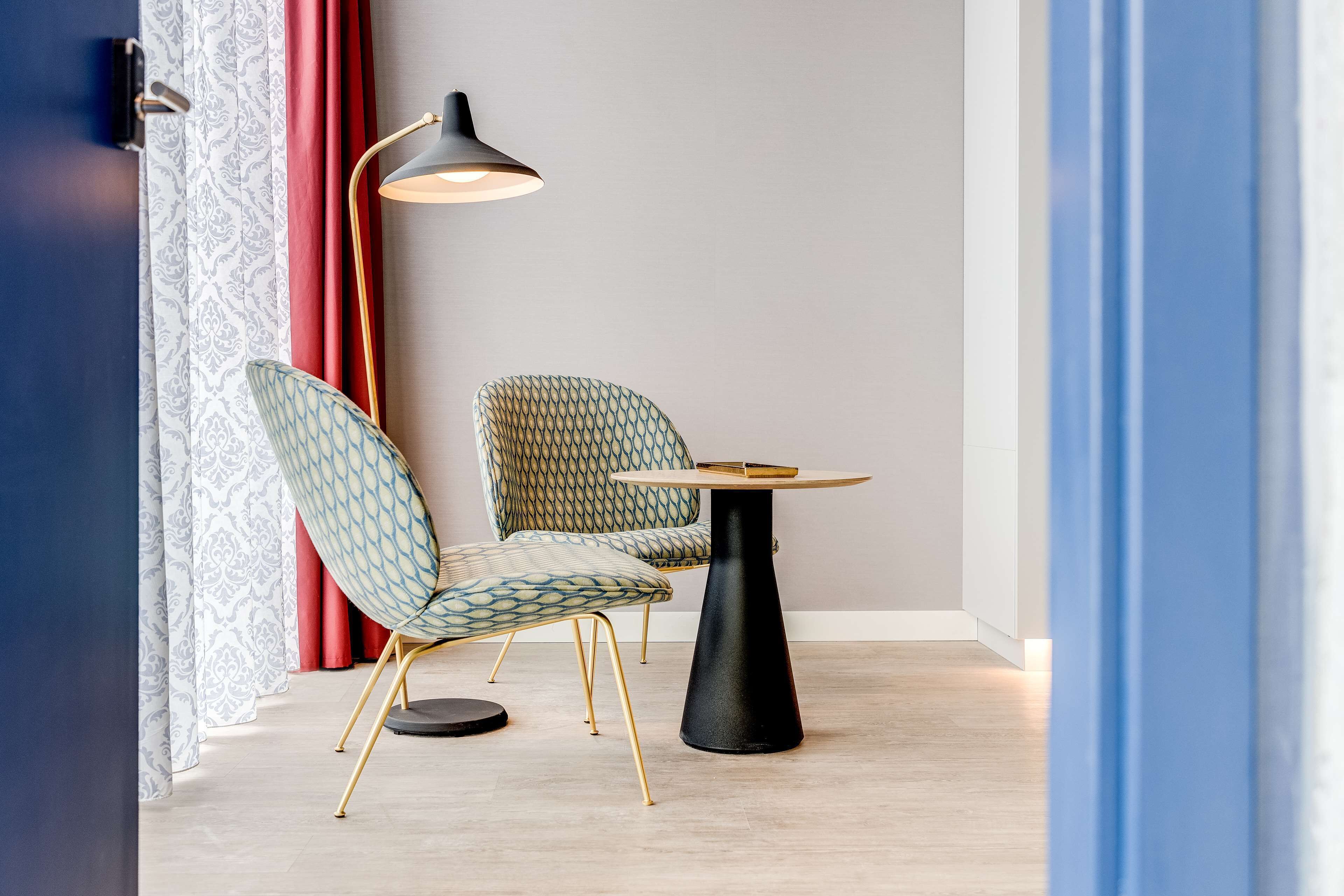 Una habitación moderna con sillas estampadas, una mesa redonda y una lámpara de pie.