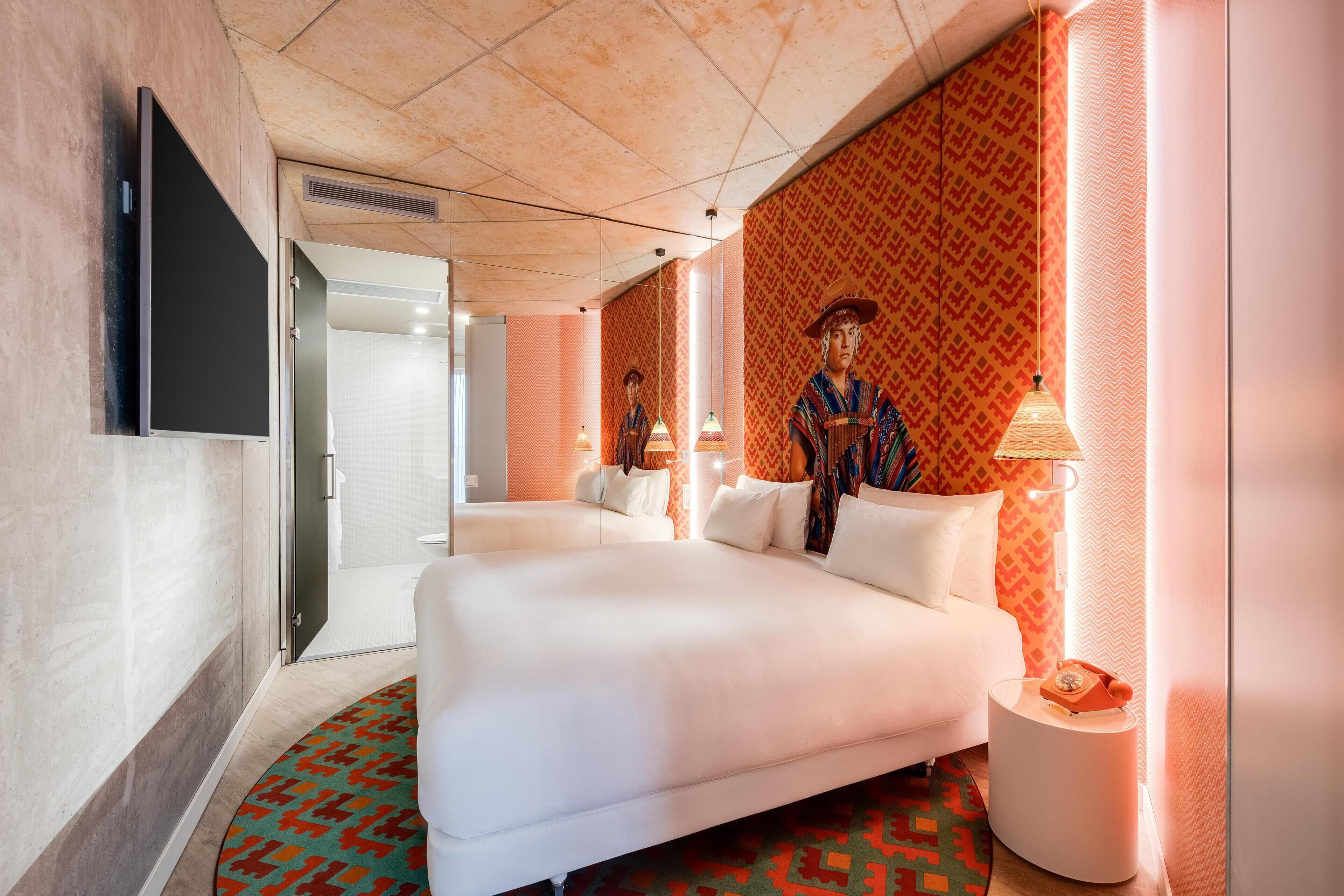 A hotel room with a large bed, bedside tables, a TV, and patterned wallpaper.