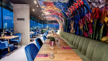 A restaurant with a long wooden table, blue chairs, and a green cushioned bench.